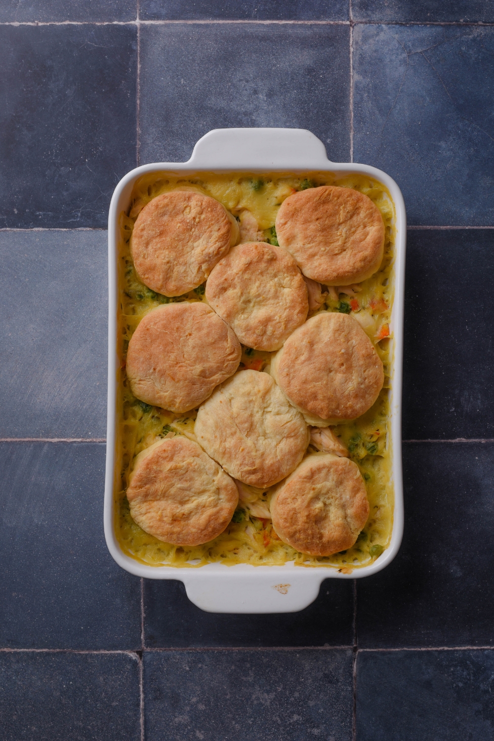 A white casserole dish of cooked chicken pot pie with eight golden brown biscuits on top.