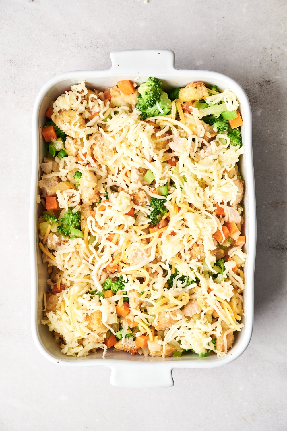 A casserole dish of chicken broccoli stuffing with shredded cheese on top.