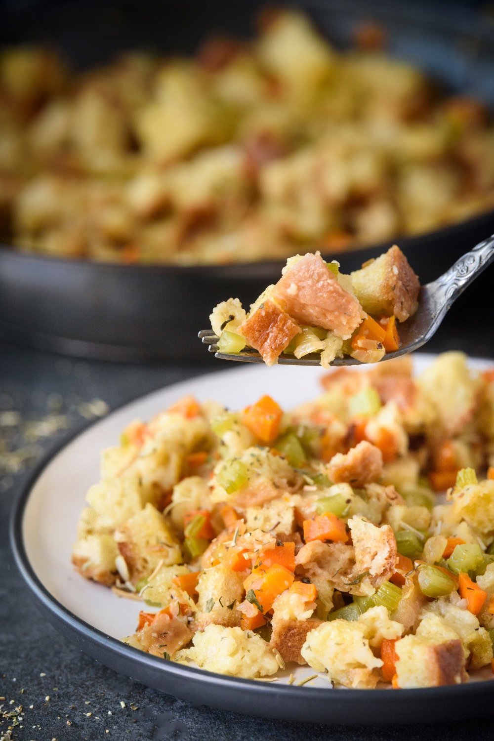 A fork holding a bite of stovetop stuffing above a plate filled with stuffing.