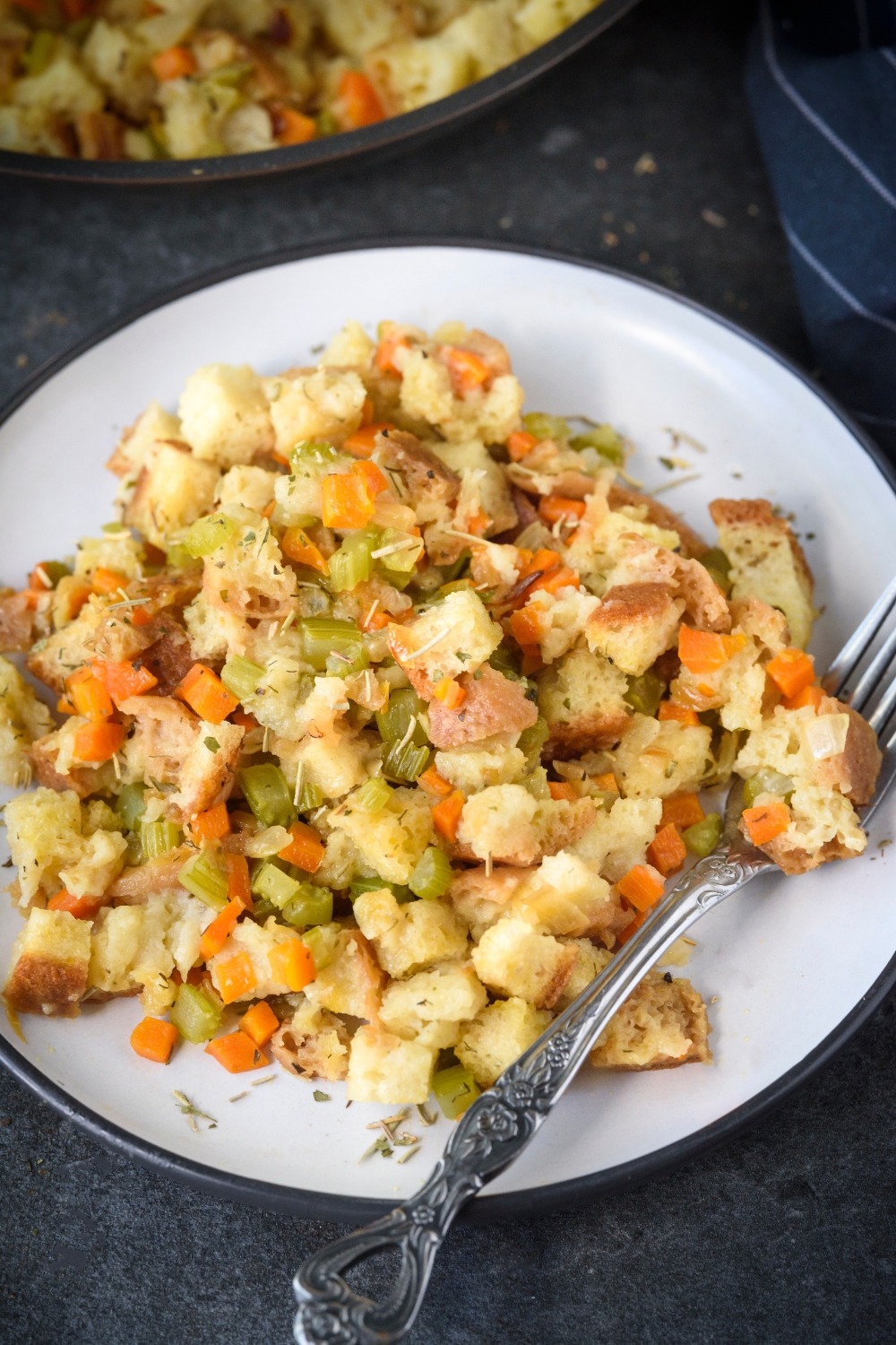 A plate of stovetop stuffing with diced celery and carrots mixed in with the stuffing. There is a fork on the plate.