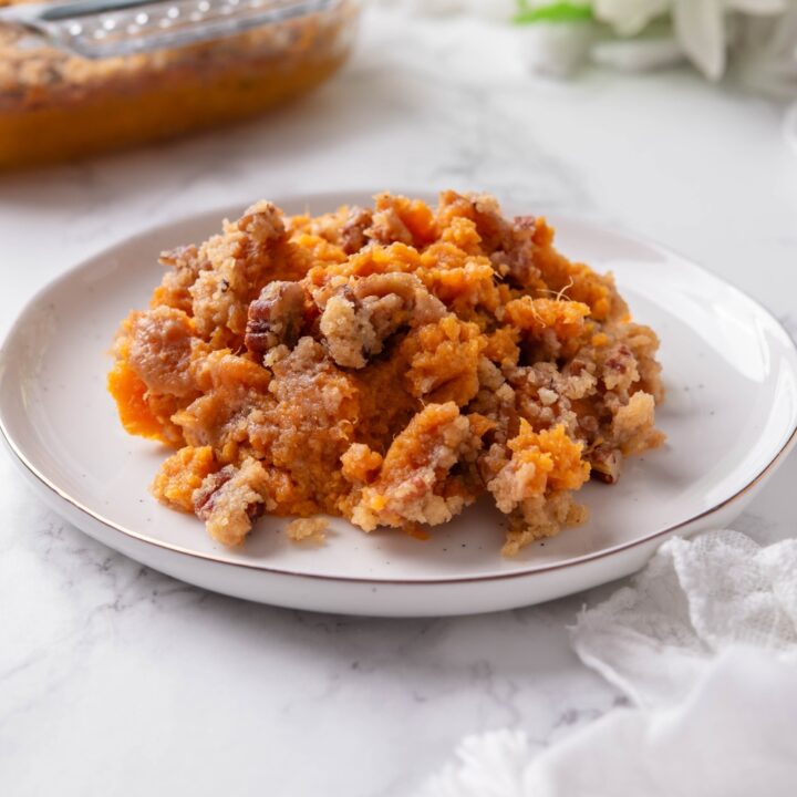 A plate filled with sweet potato casserole mixed with pecans and brown sugar. The rest of the casserole is in the background.