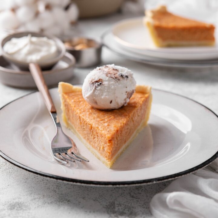 A slice of sweet potato pie on a plate with a dollop of whipped cream on top and a fork on the plate next to it.