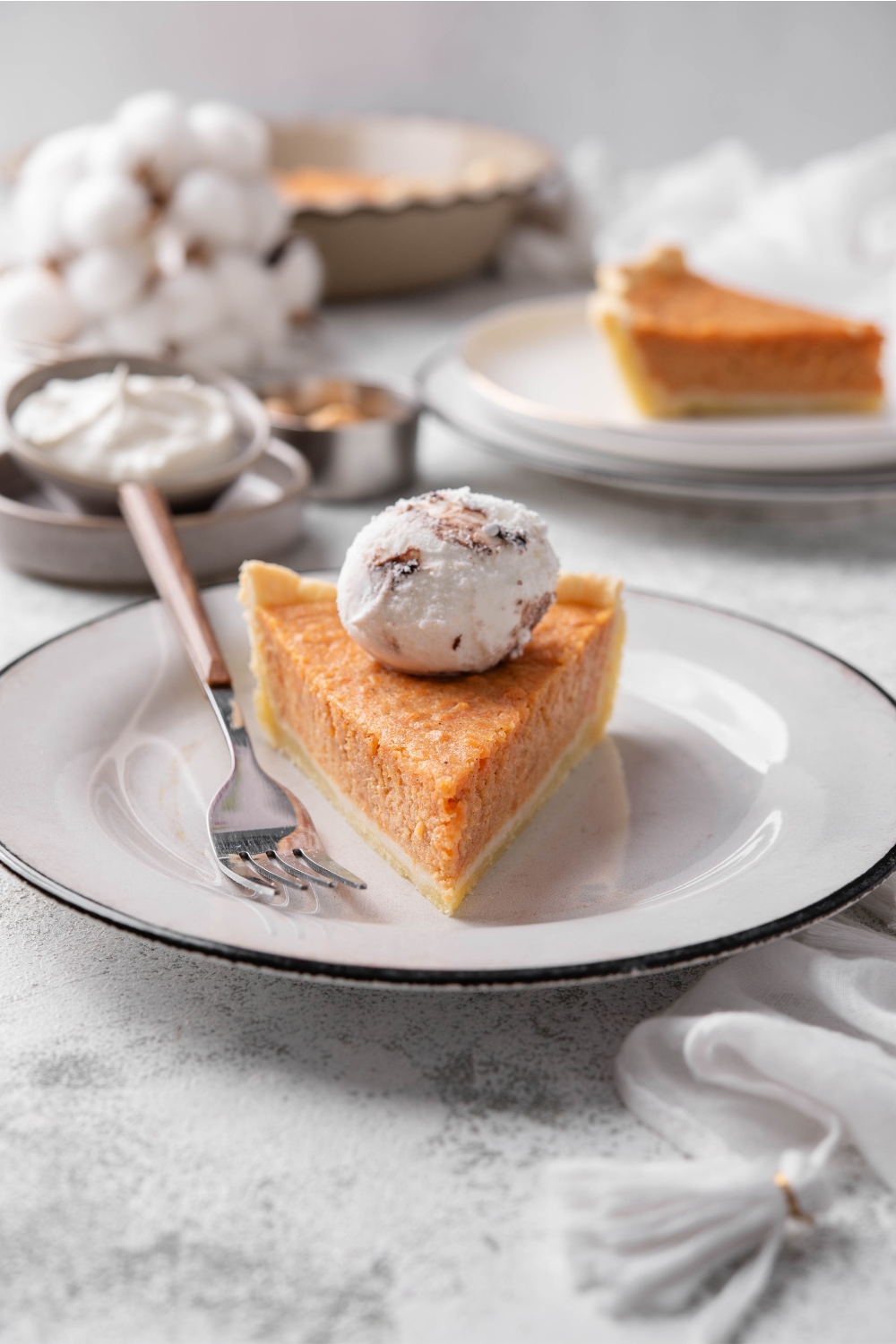 A slice of sweet potato pie on a plate with a dollop of whipped cream on top and a fork on the plate next to it.