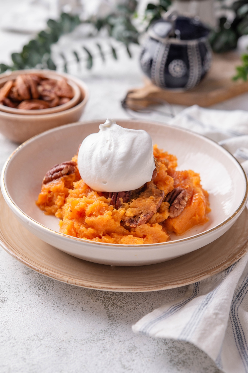 A bowl filled with sweet potato pudding mixed with pecans and a dollop of whipped cream is on top.