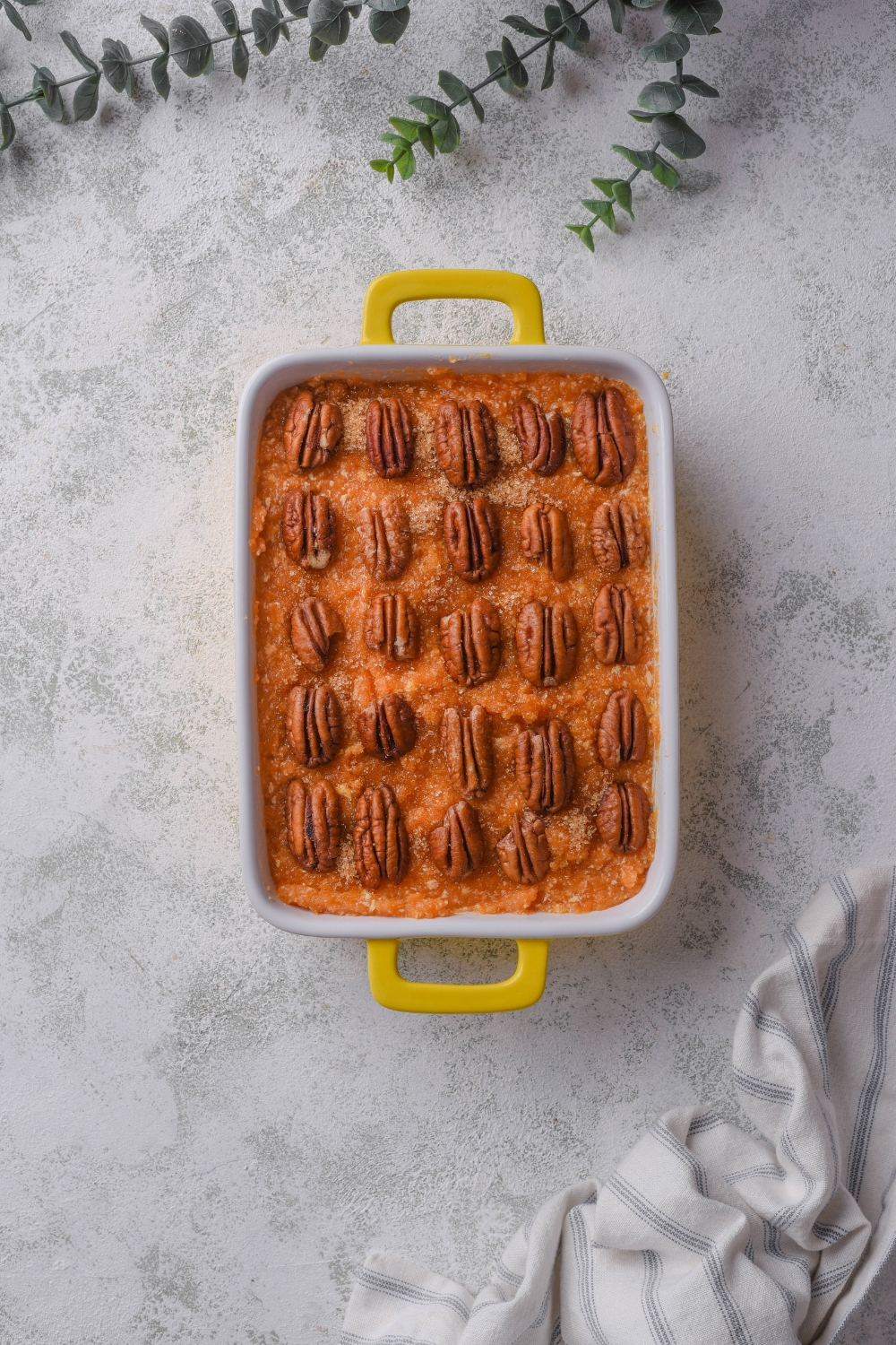 A baking dish filled with sweet potato pudding topped with pecans and brown sugar.