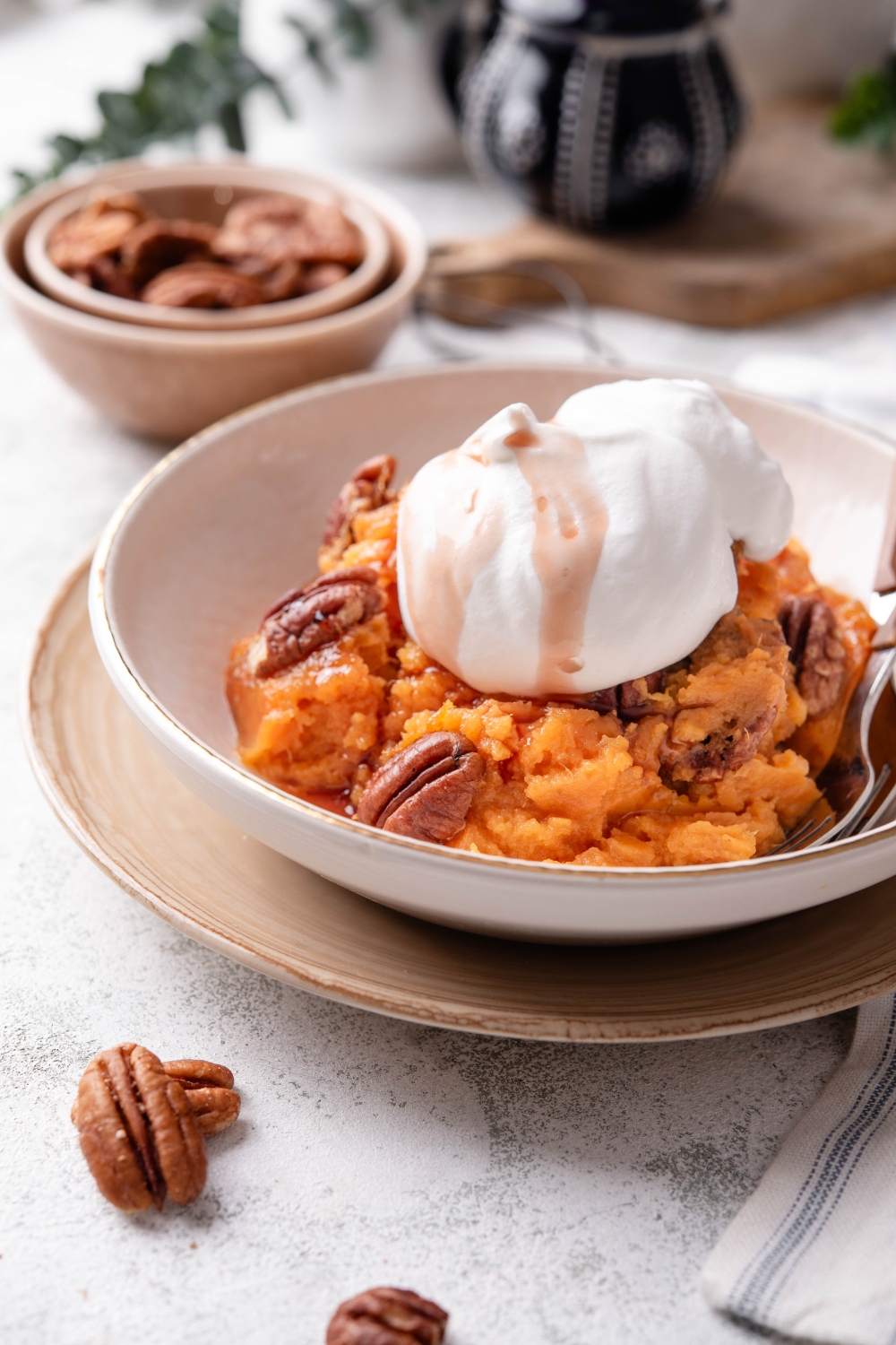 A bowl filled with sweet potato pudding mixed with pecans and a dollop of whipped cream is on top.