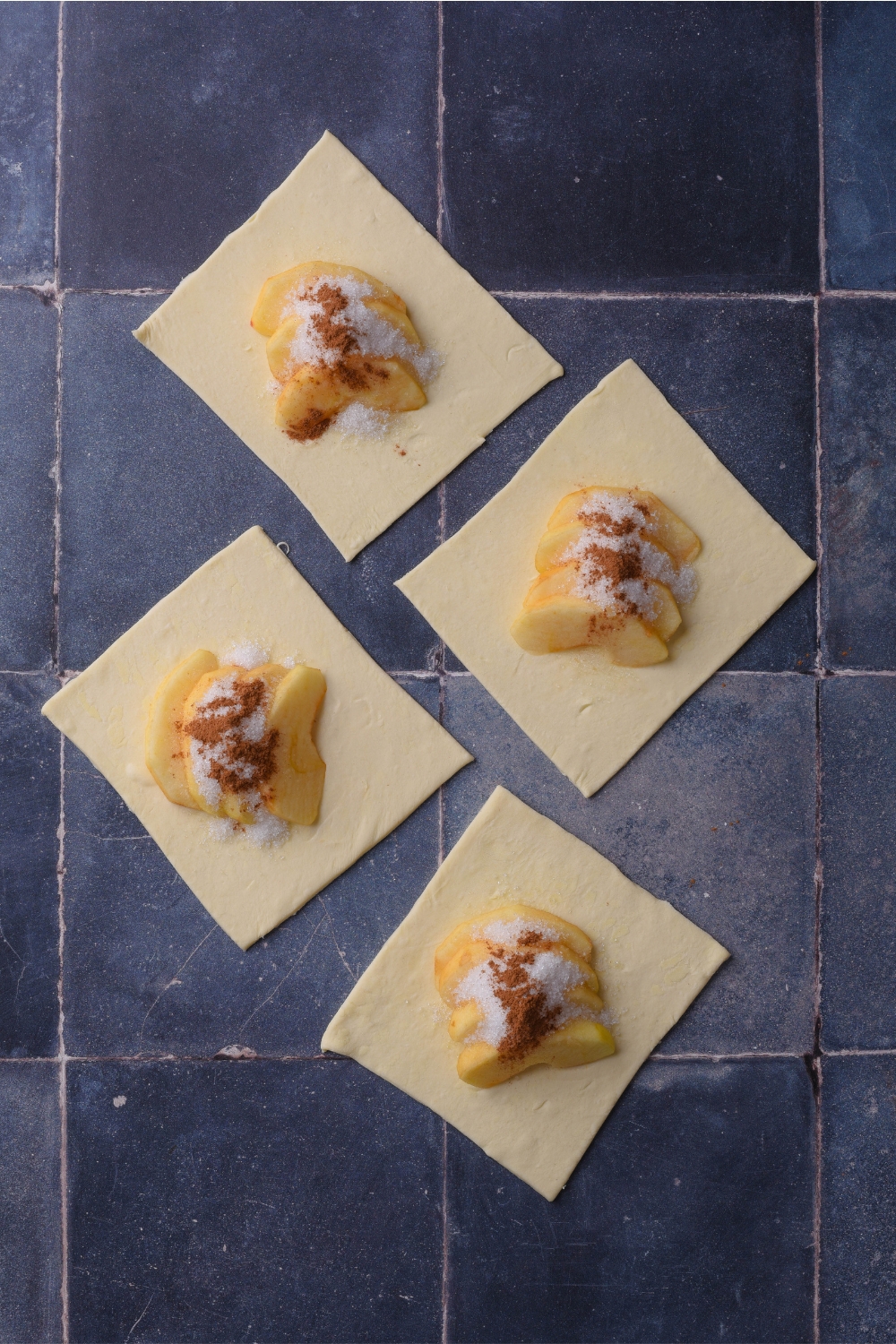 Apples, cinnamon, and sugar being added to the pastry dough squares.