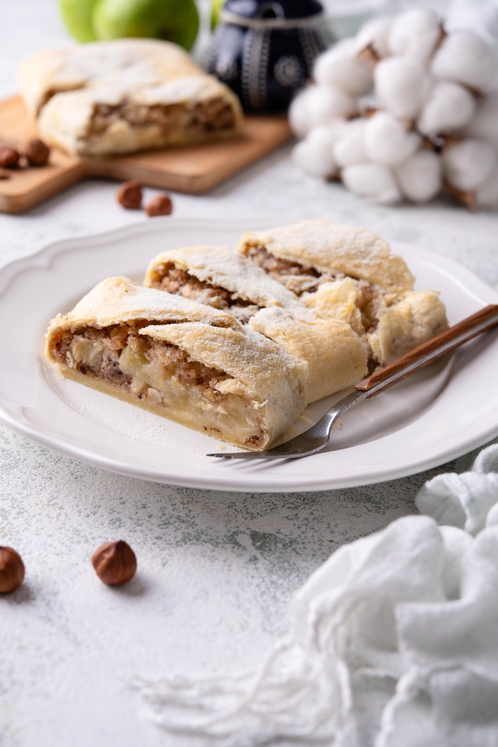 A plate of sliced apple strudel garnished with powdered sugar and served with a fork.