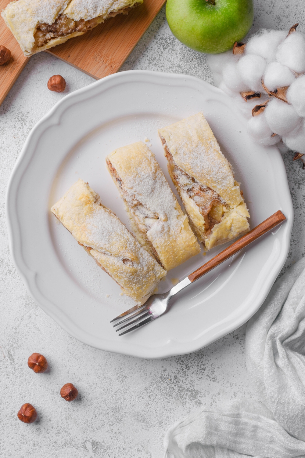 Overhead view of sliced apple strudel dusted with powdered sugar and served with a fork.