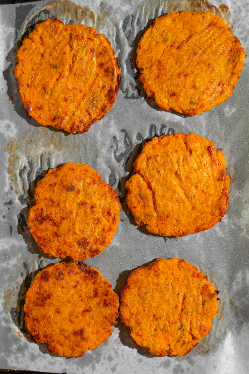 Two rows of three sweet potato patties on top of parchment paper on a baking sheet.