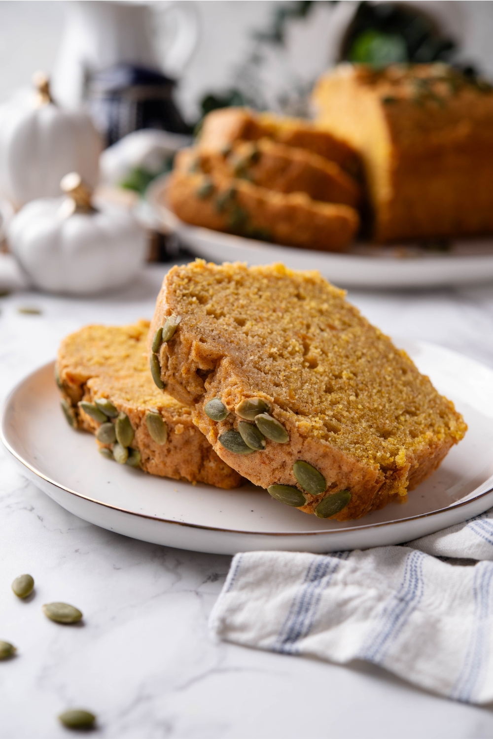 A plate with two slices of pumpkin bread topped with pumpkin seeds.
