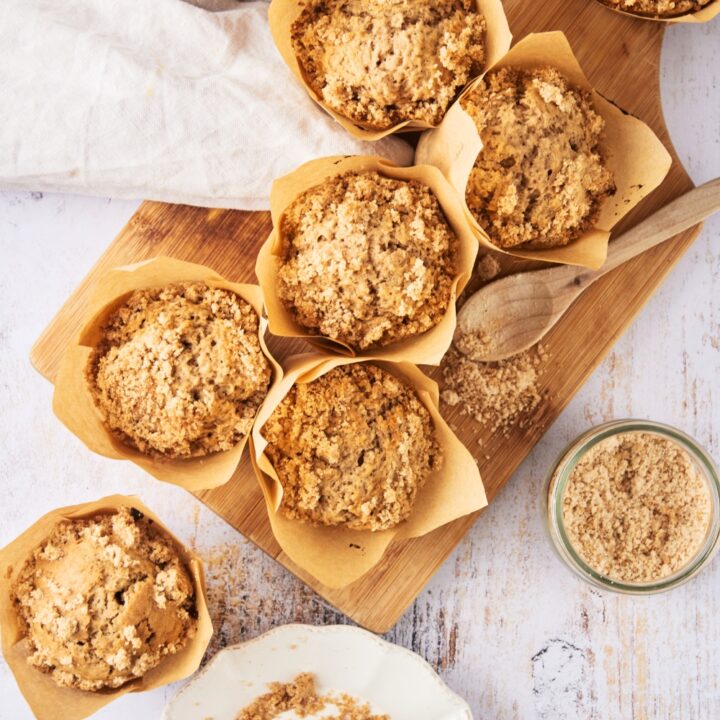 Six muffins in parchment paper on top of a wooden cutting board on a white counter.