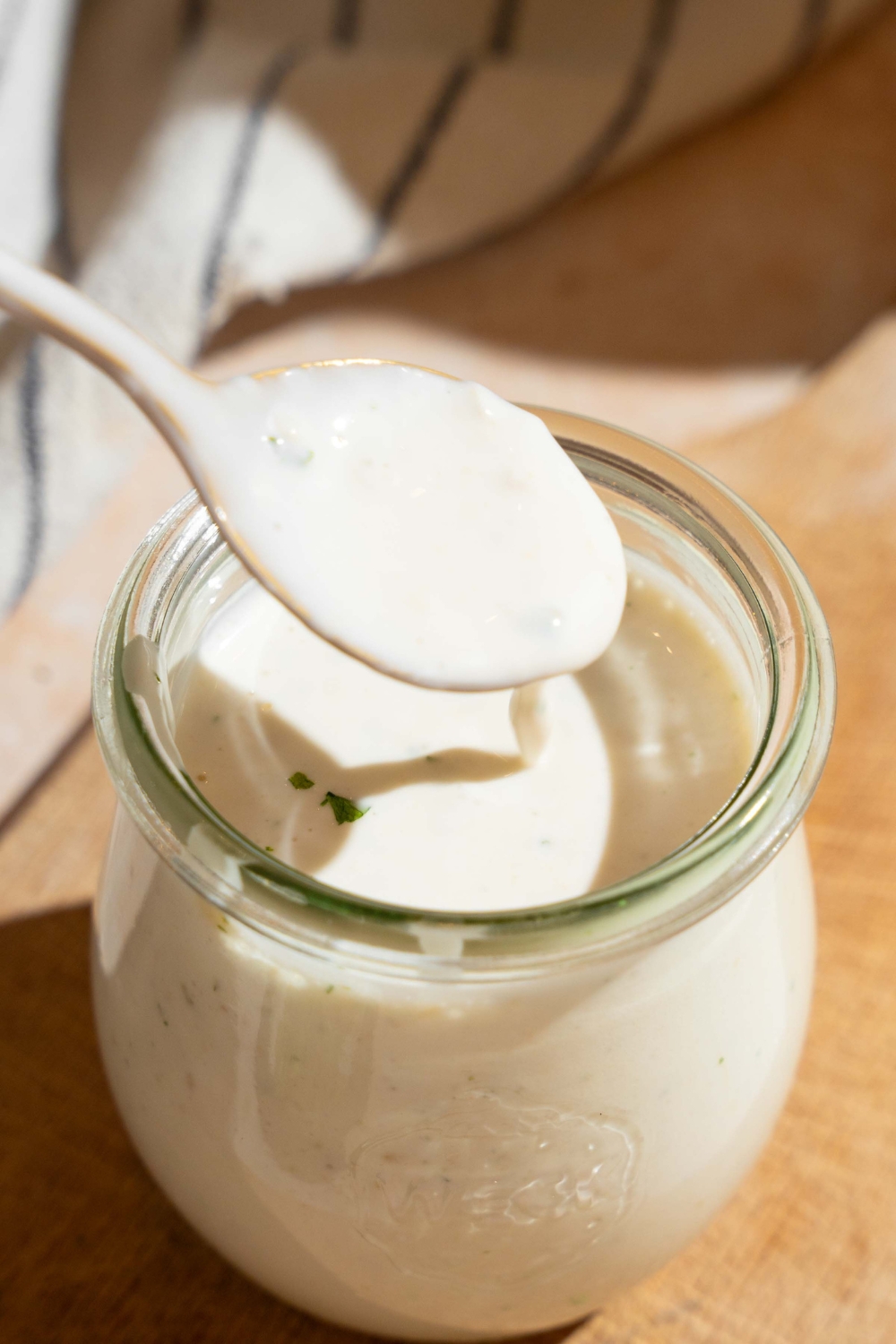A spoon with wingstop ranch covering it and dripping down into a glass jar with the ranch in it.