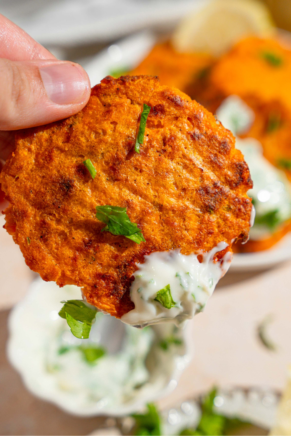 A hand holding a sweet potato patty with some herb mayo on it.