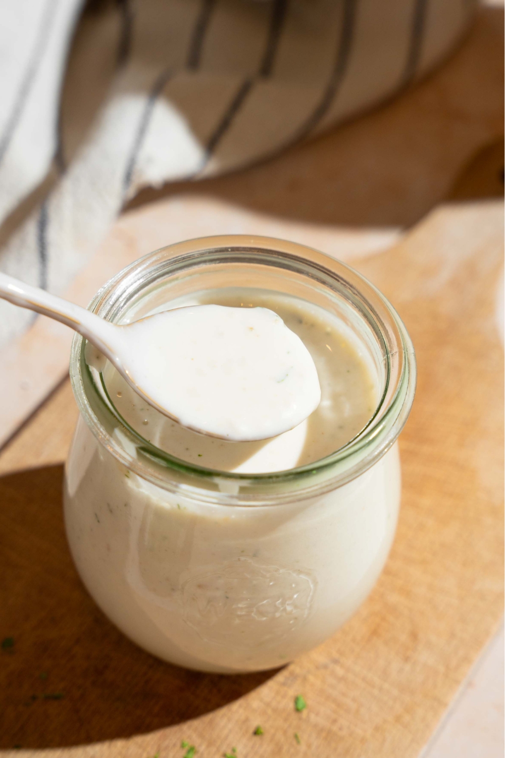 A spoon with wingstop ranch over it lifted out of a glass jar with the ranch in it.