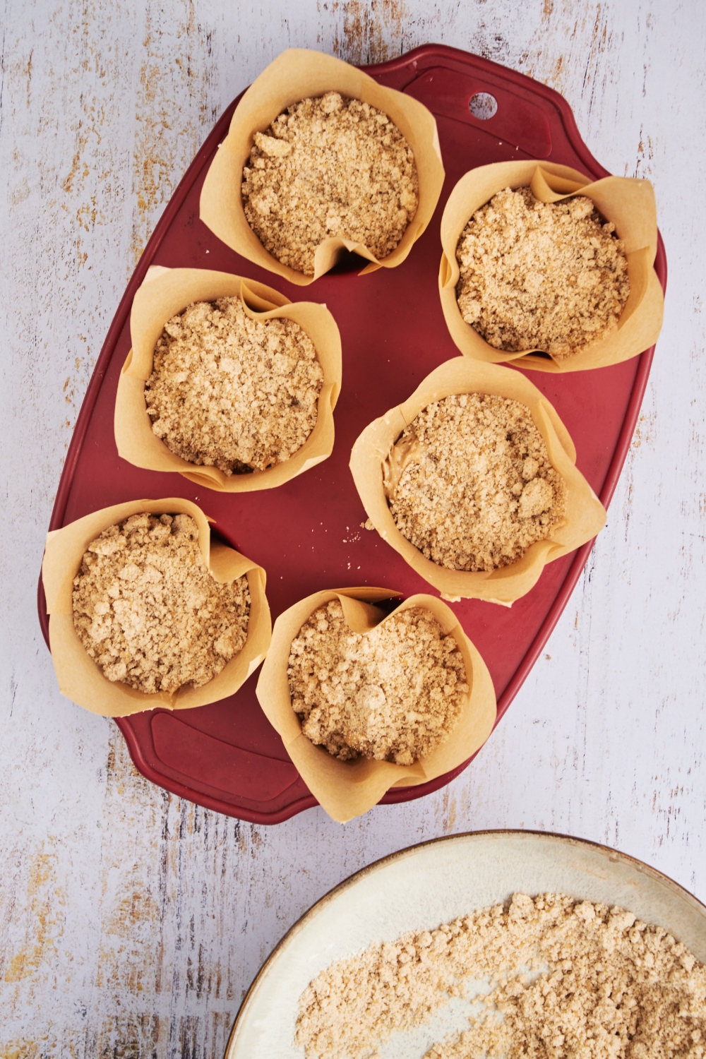 A muffin baking tray with unbaked muffins topped with cinnamon streusel topping.