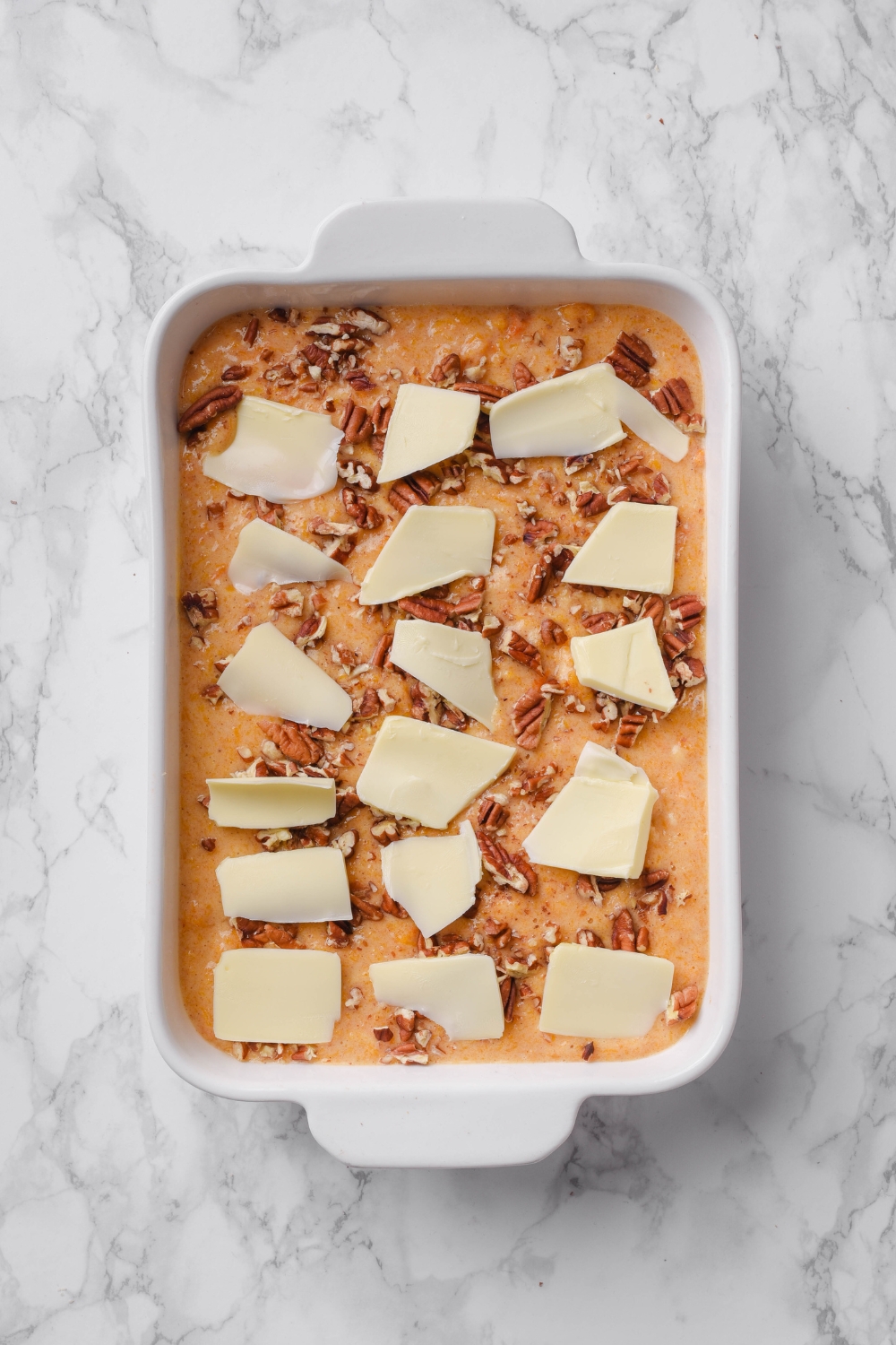 A casserole dish with pumpkin dump cake batter topped with pecans and butter.