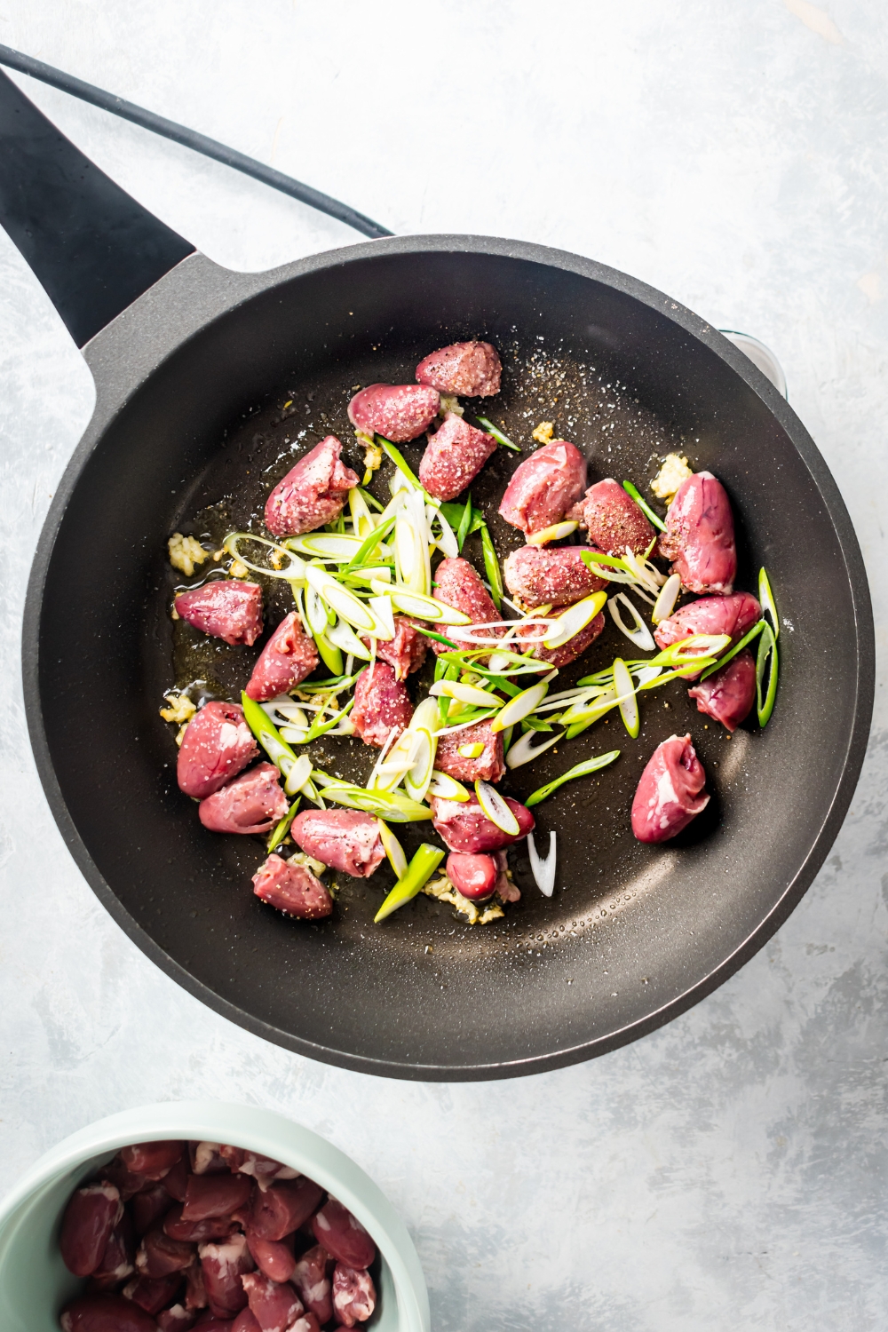 Green onion on top of raw chicken hearts in a skillet.