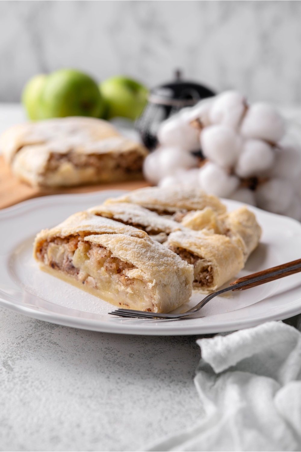 Puff pastry apple strudel sliced into three portions and served on a plate with a fork.