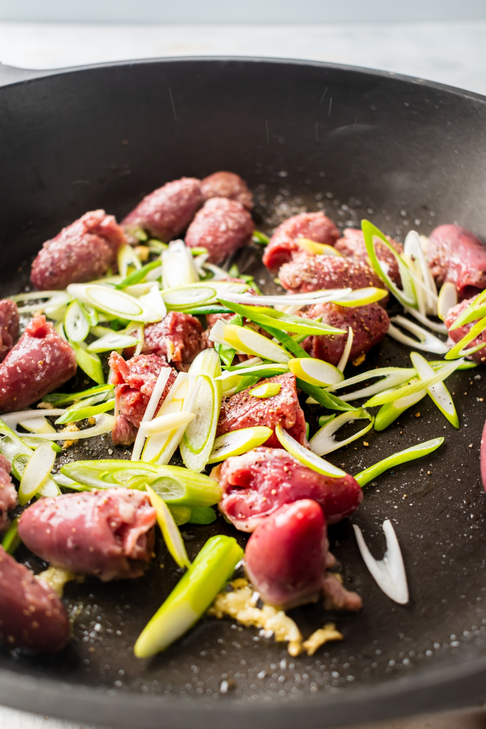 Green onion and raw chicken hearts in a skillet.