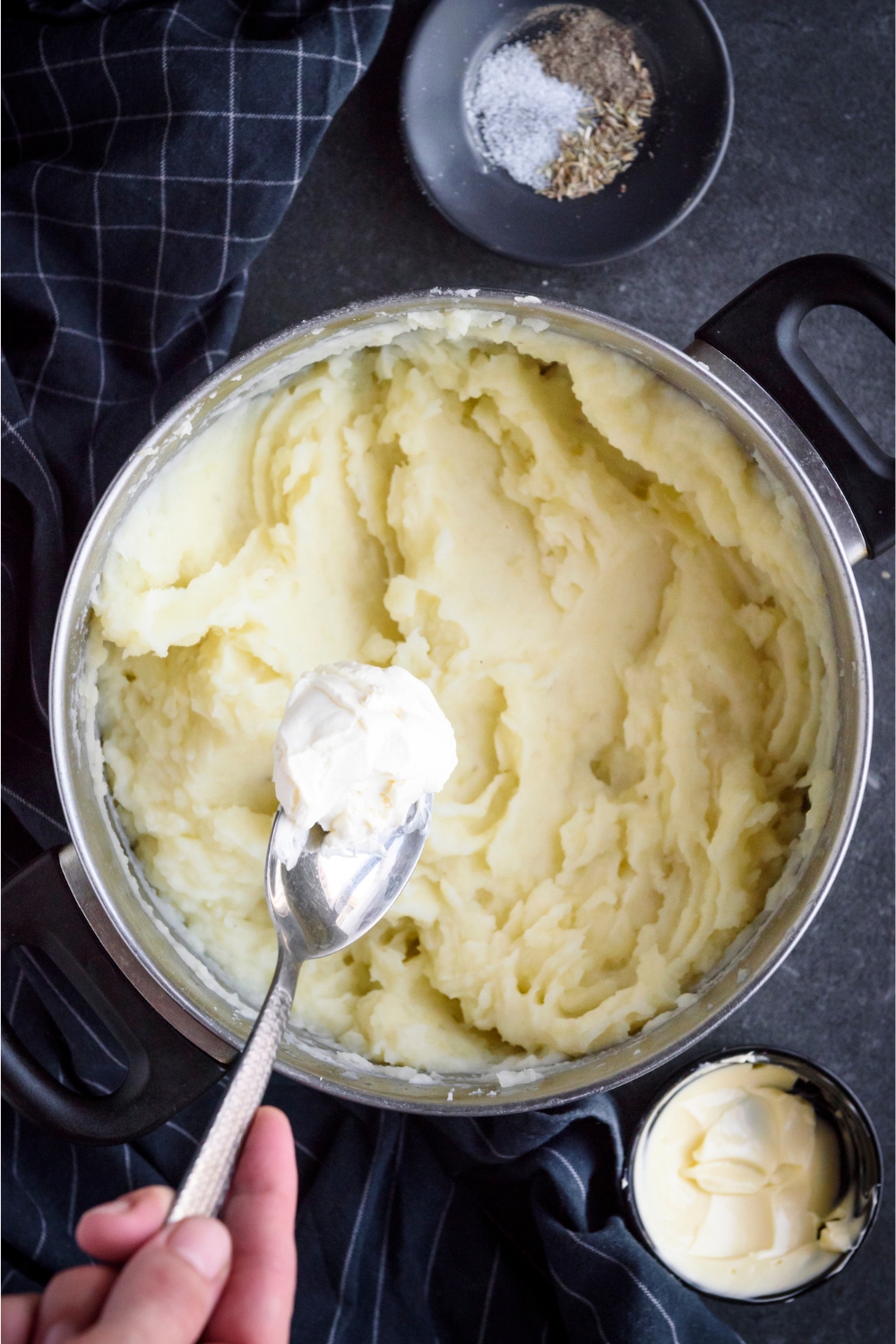 Someone dropping a spoonful of sour cream into a large pot of mashed potatoes.