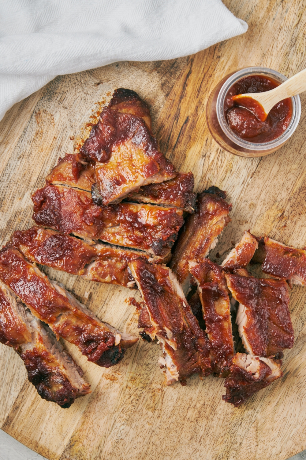Riblets on top of a wooden cutting board with a glass jar of bbq sauce next to them.