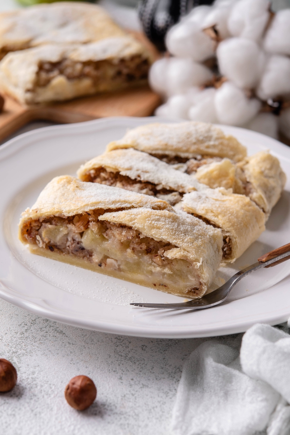 An apple strudel cut into three slices on a white plate that is on top of a grey counter.