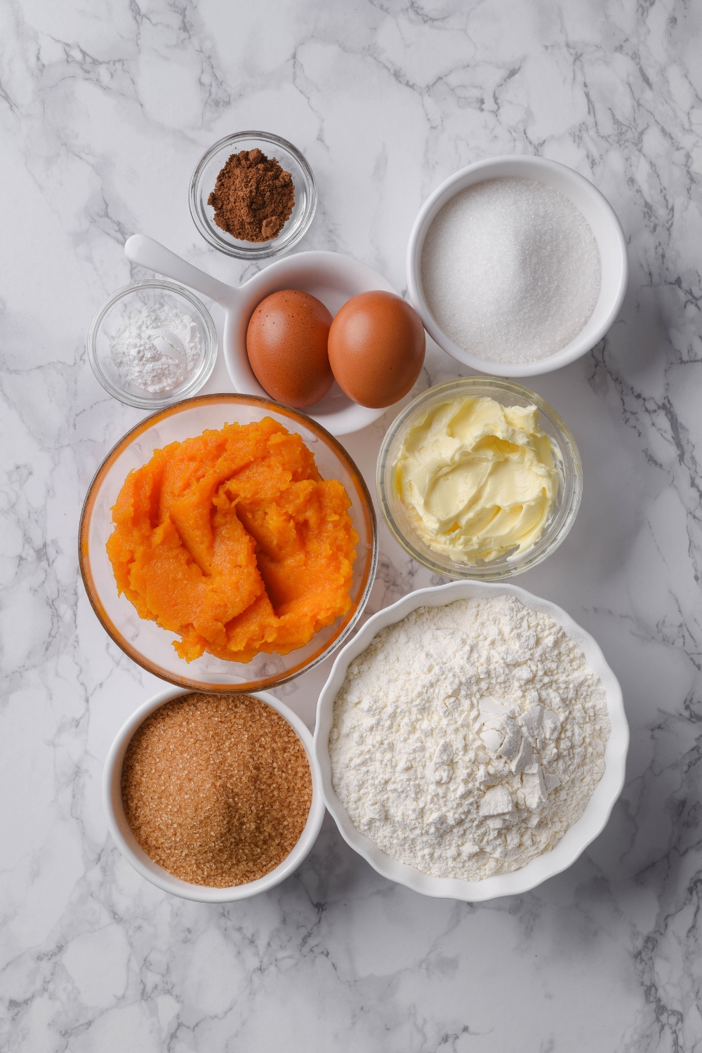 A countertop with pumpkin puree, butter, flour, sugar, brown sugar, eggs, baking powder, spices.