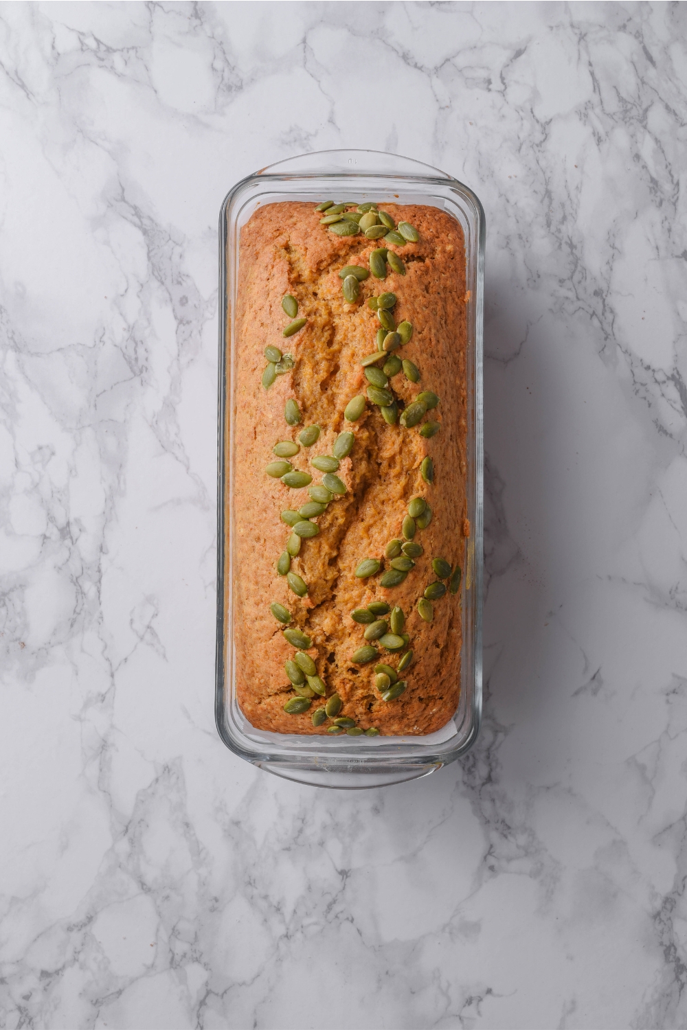 A loaf pan with baked pumpkin loaf topped with pumpkin seeds.