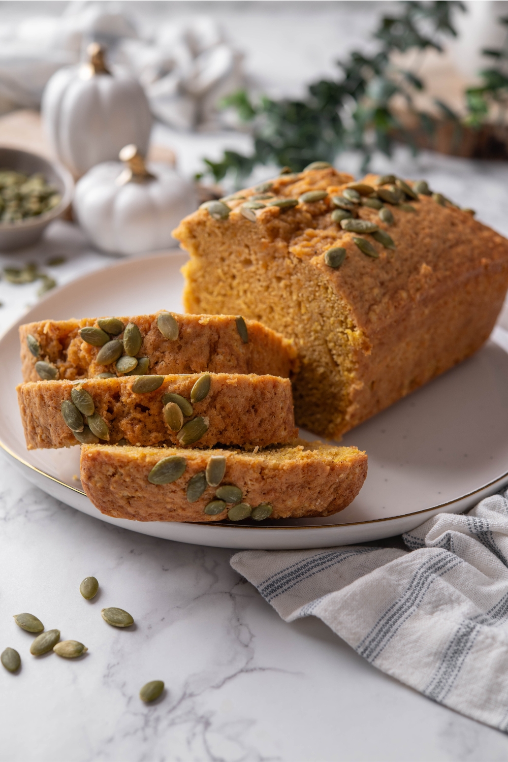 A plate with half the pumpkin loaf sliced and the remaining loaf behind the slices.