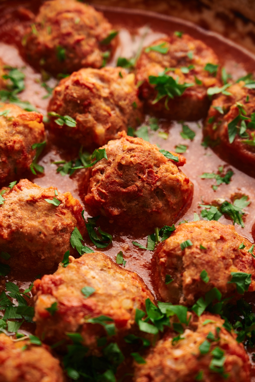 a pot of cooked meatballs in a red sauce with parsley