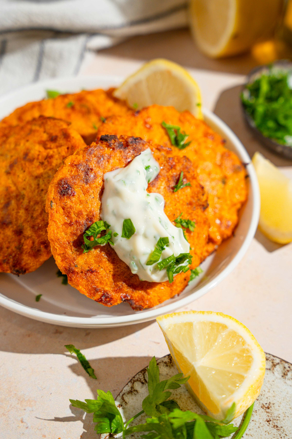An herbed mayo on top of a sweet potato patty with more sweet potato patties behind it on a white plate.