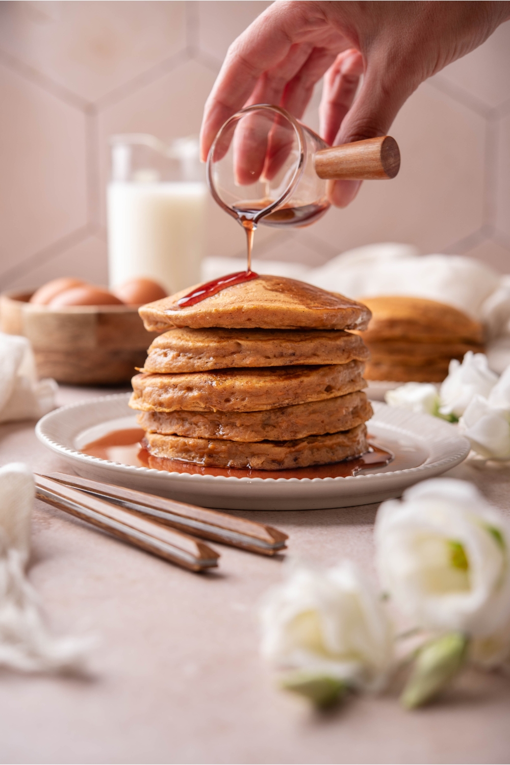 A plate with a stack of sweet potato pancakes. Maple syrup is being poured onto them.