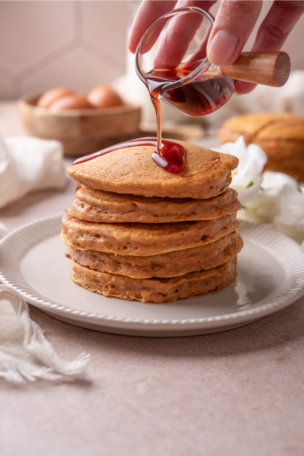 A plate with a stack of sweet potato pancakes. Maple syrup is being poured onto them.