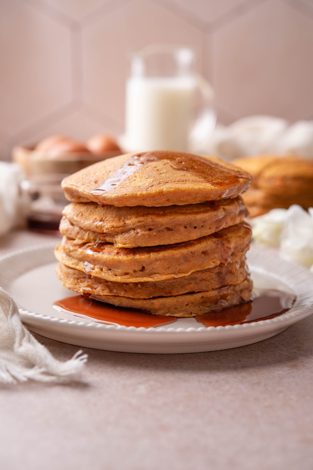 A plate with a stack of sweet potato pancakes with syrup drizzled over them.