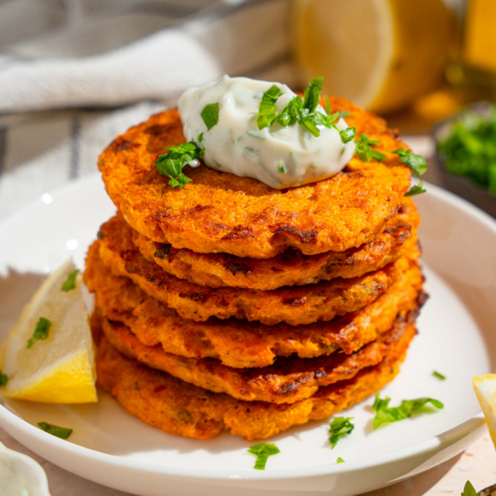 Herbed mayo on top of a stack of six sweet potato patties on a white plate.