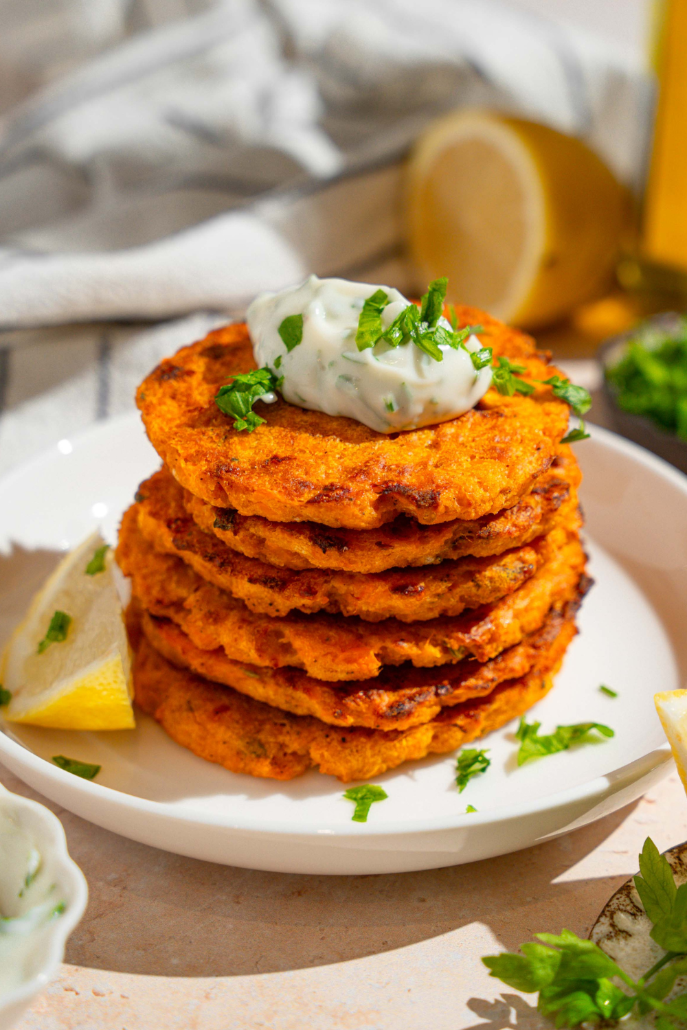 Herbed mayo on top of a stack of six sweet potato patties on a white plate.