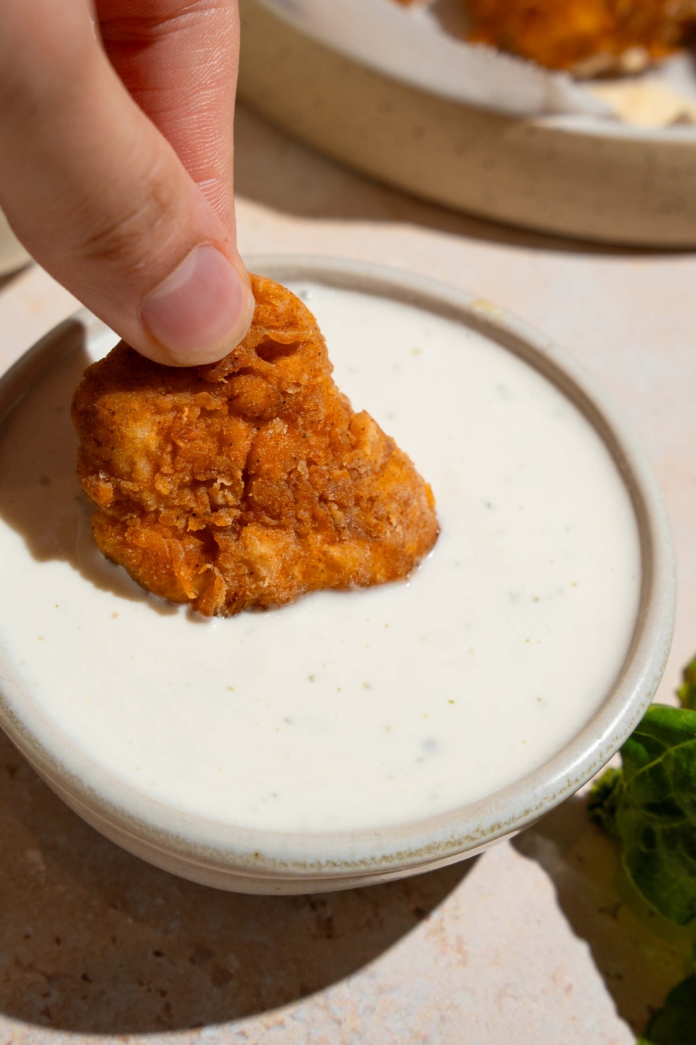 A hand dipping a chicken nugget into wingstop ranch that is in a white bowl.