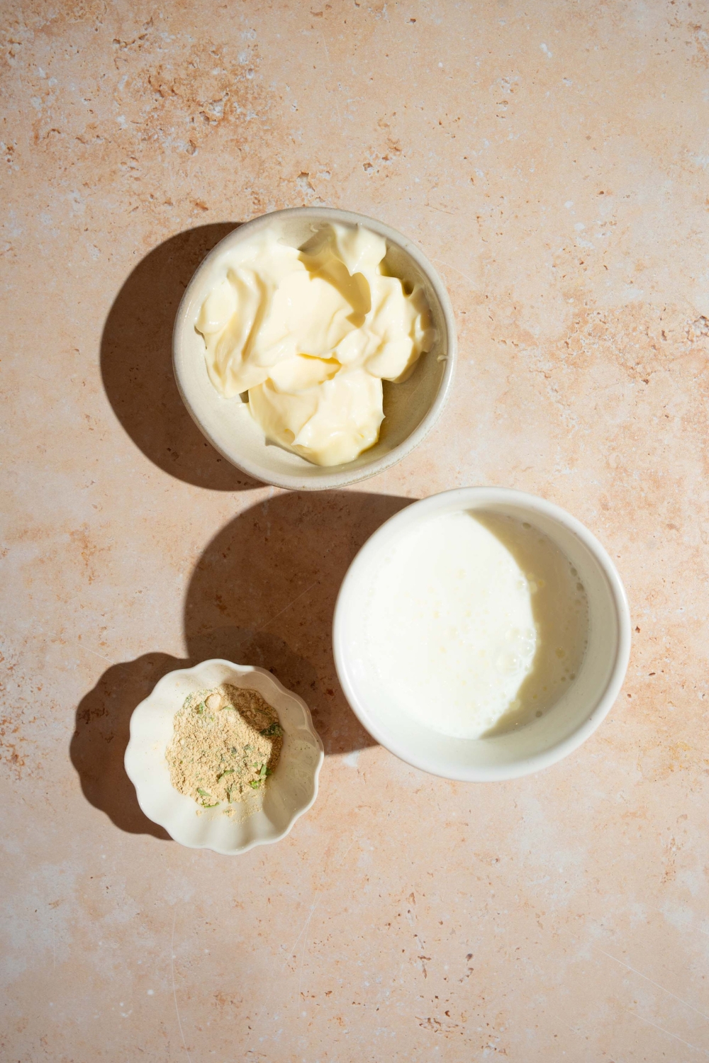 A bowl of mayo, a bowl of buttermilk, and a bowl of ranch dressing all on a white counter.