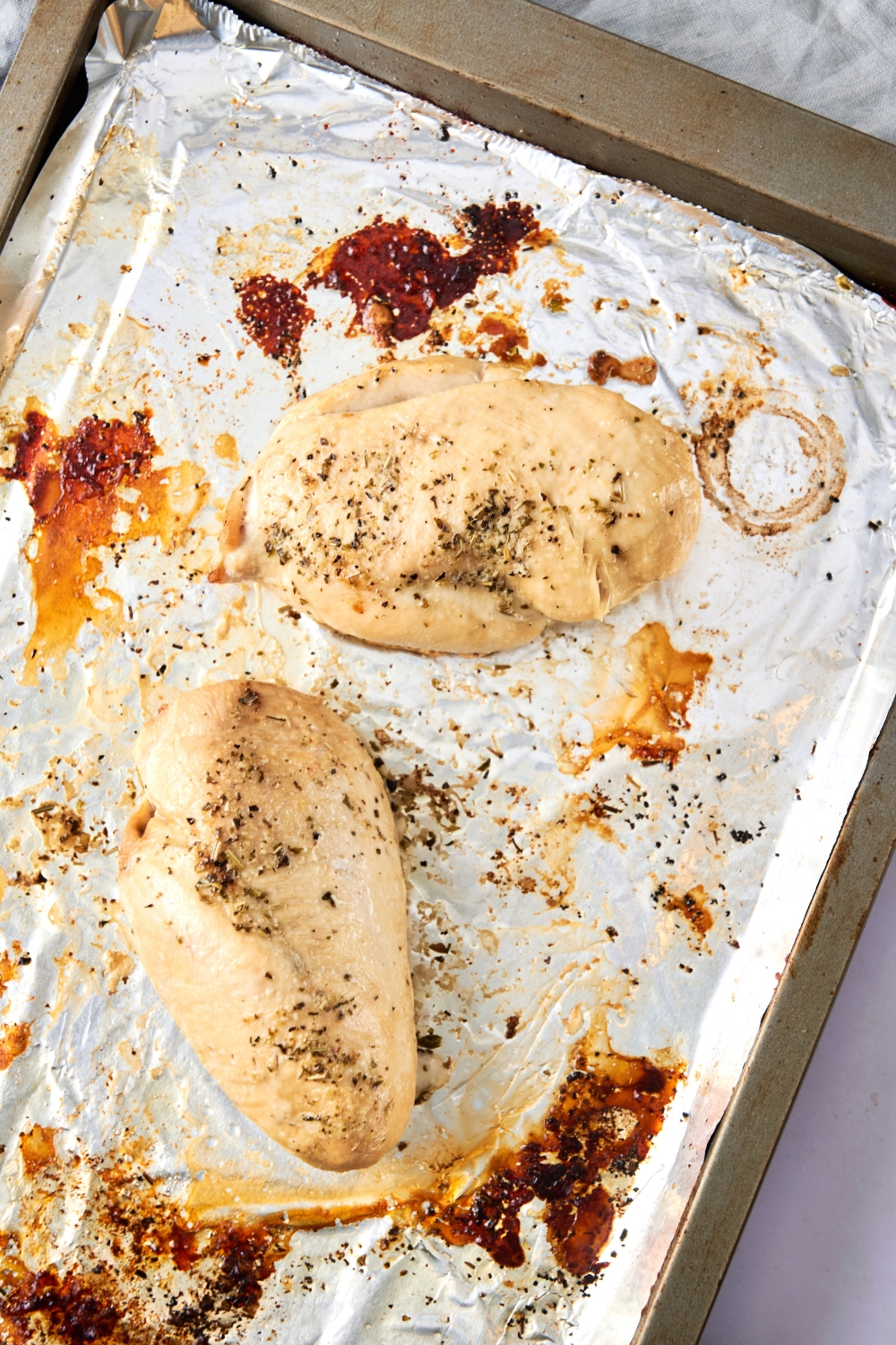 Two baked chicken breasts are on a foil lined baking sheet.