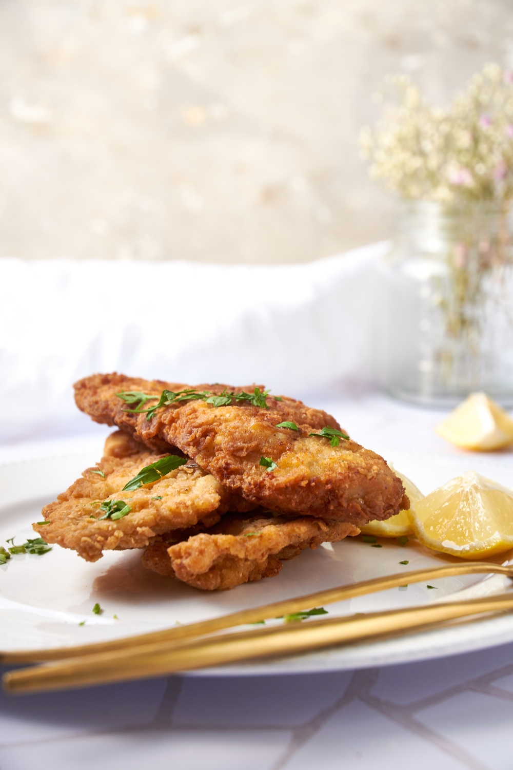 Three pieces of fried chicken stacked on top of each other, garnished with fresh herbs and two lemon wedges.