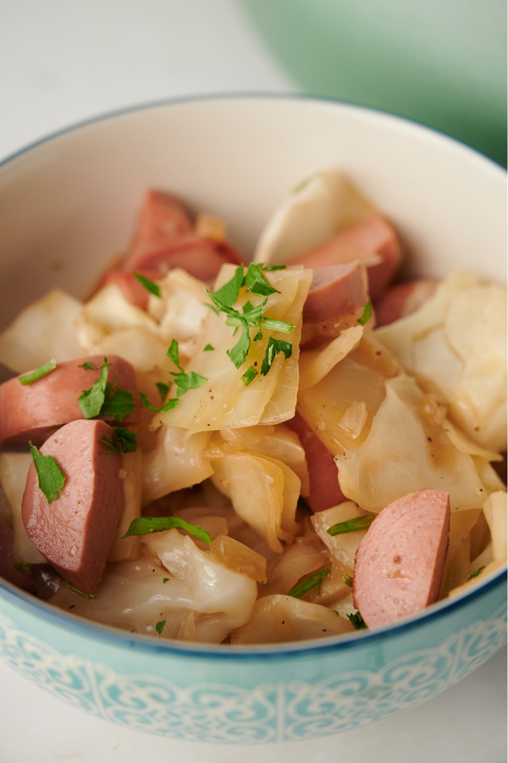 A bowl of sausage and cabbage topped with fresh green herbs.