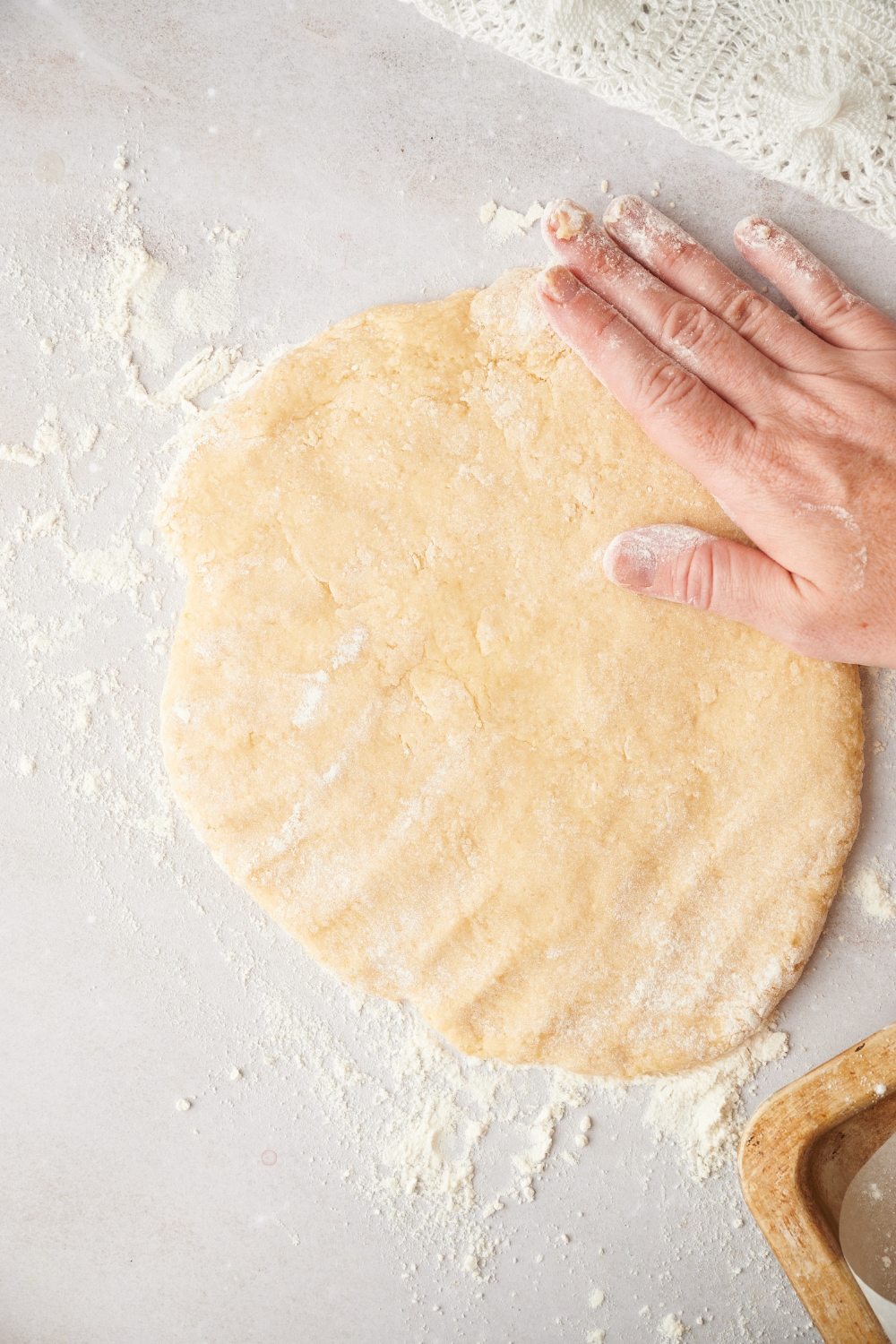 Someone smooths out the biscuit dough with their hand on a floured surface.