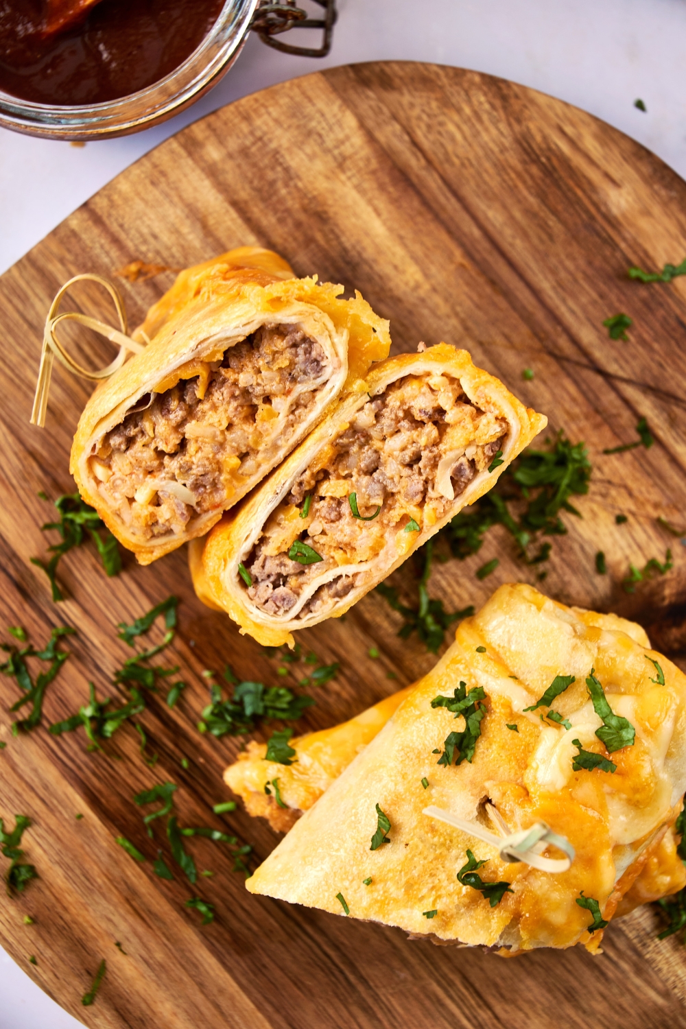 Two grilled cheese burritos sit on a wooden serving board. They have been garnished with fresh herbs.