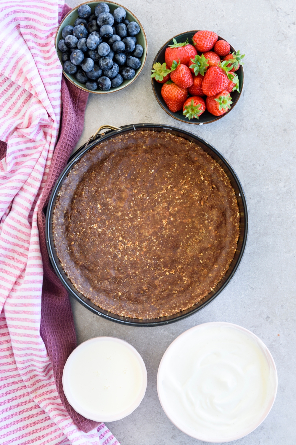 An assortment of ingredients including a chocolate pie crust and bowls of berries, yogurt, and whipped topping.