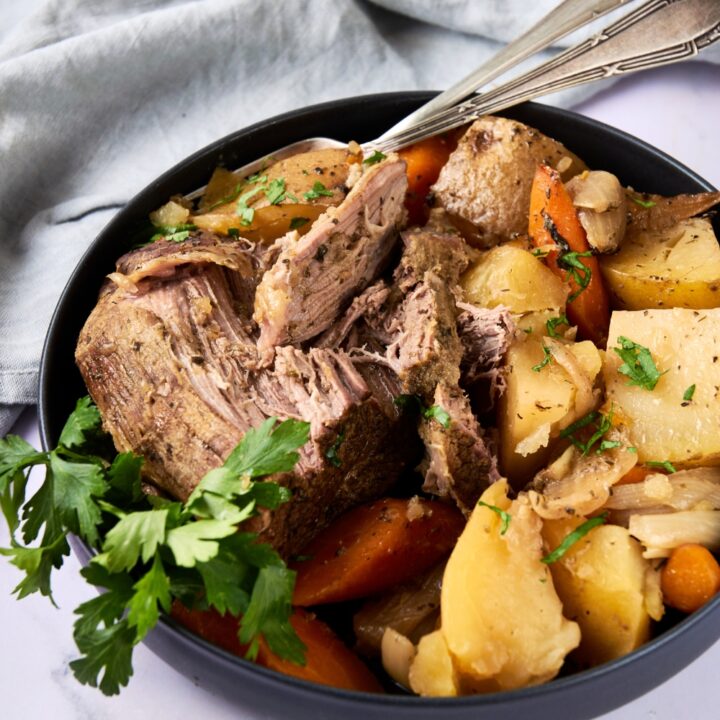 Two serving utensils sit in a full dish of roast and veggies.