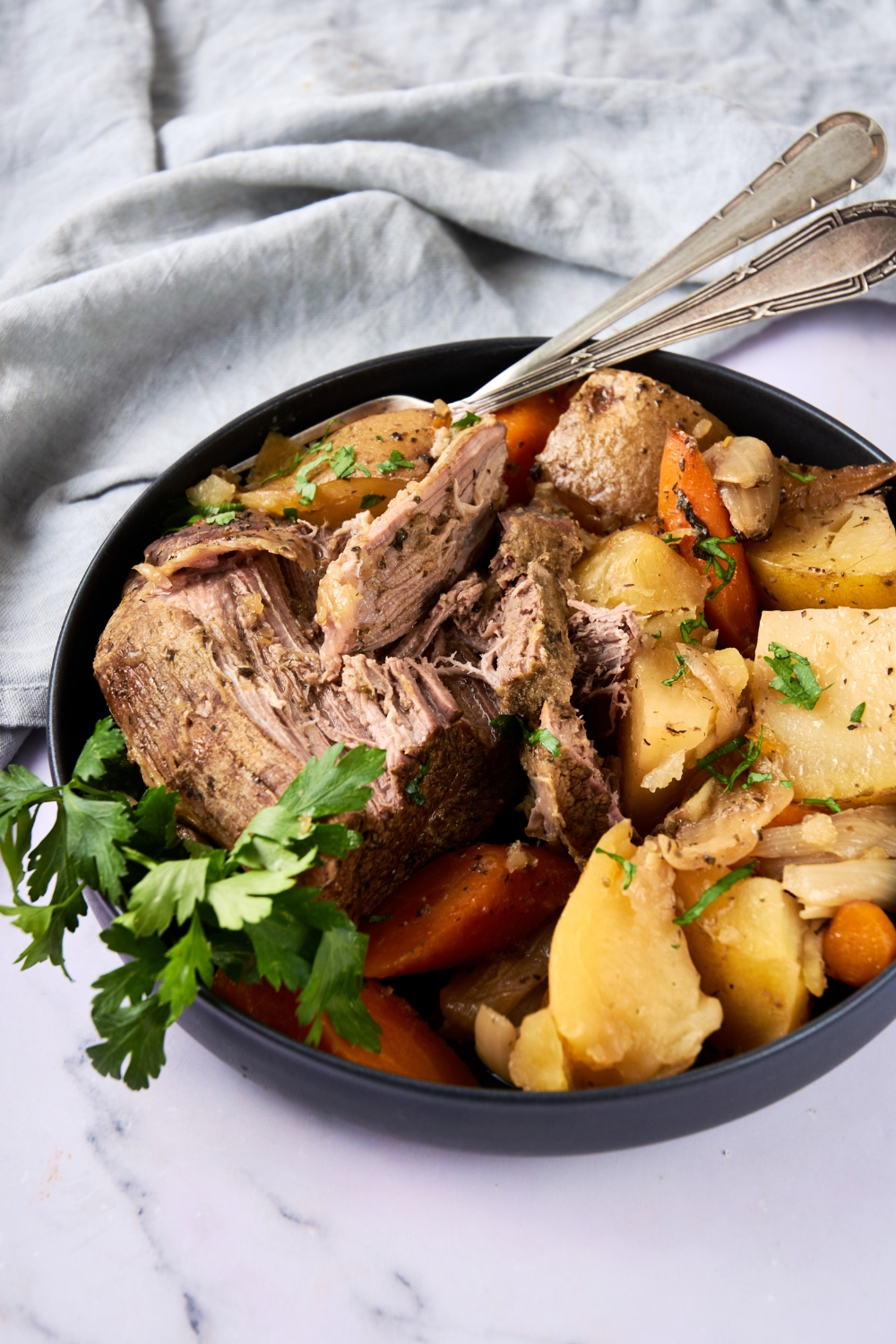 Two serving utensils sit in a full dish of roast and veggies.