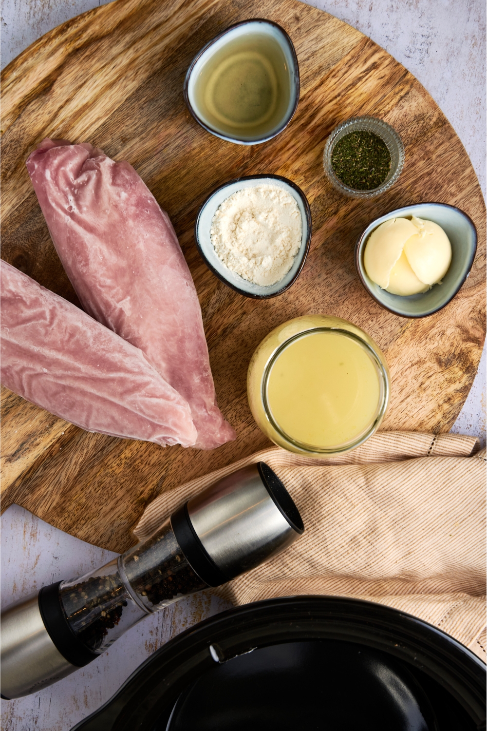 A countertop with frozen turkey, flour, butter, butter, broth, and seasonings in multiple bowls.