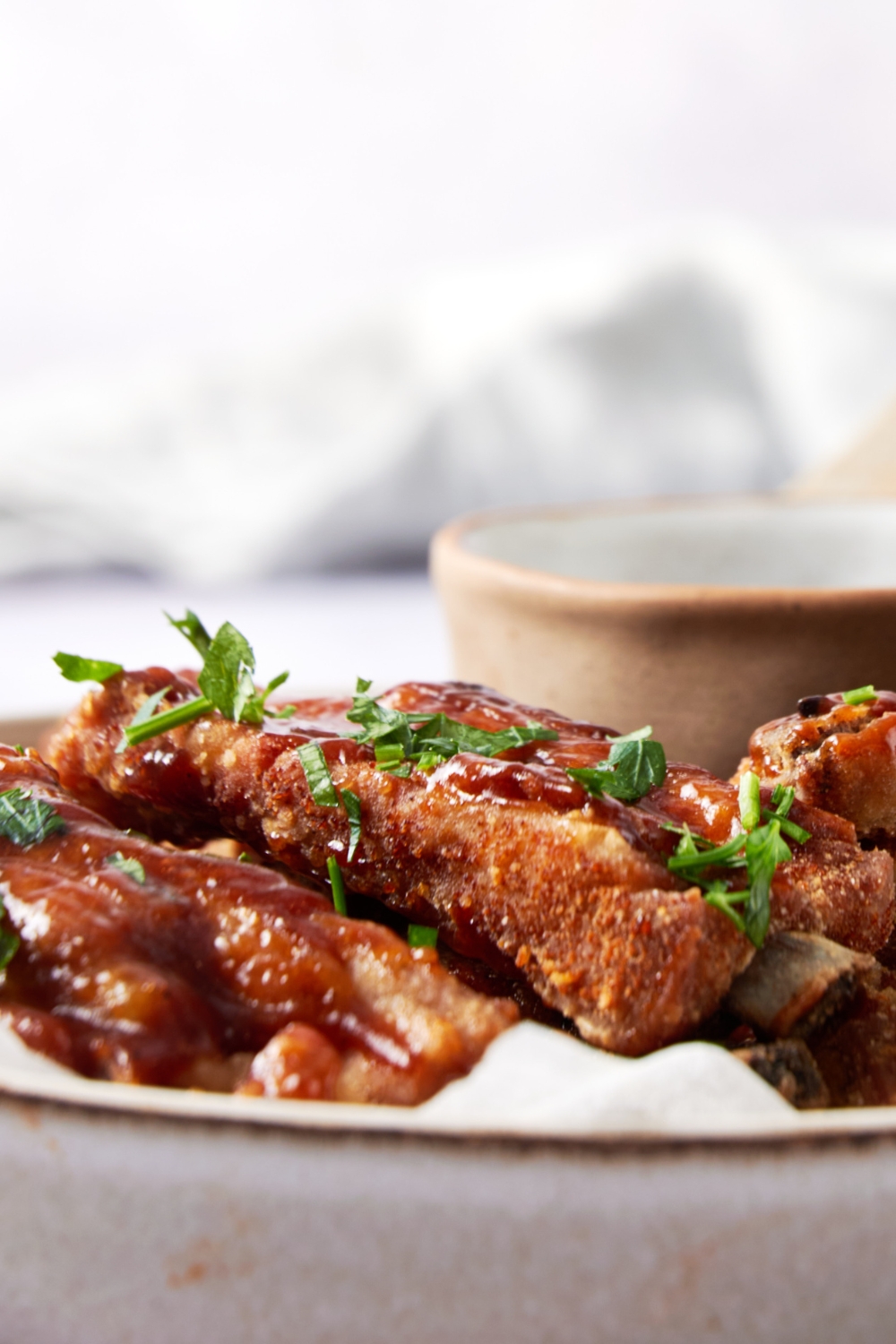 Close up of fried ribs covered in sauce and garnished with fresh herbs.