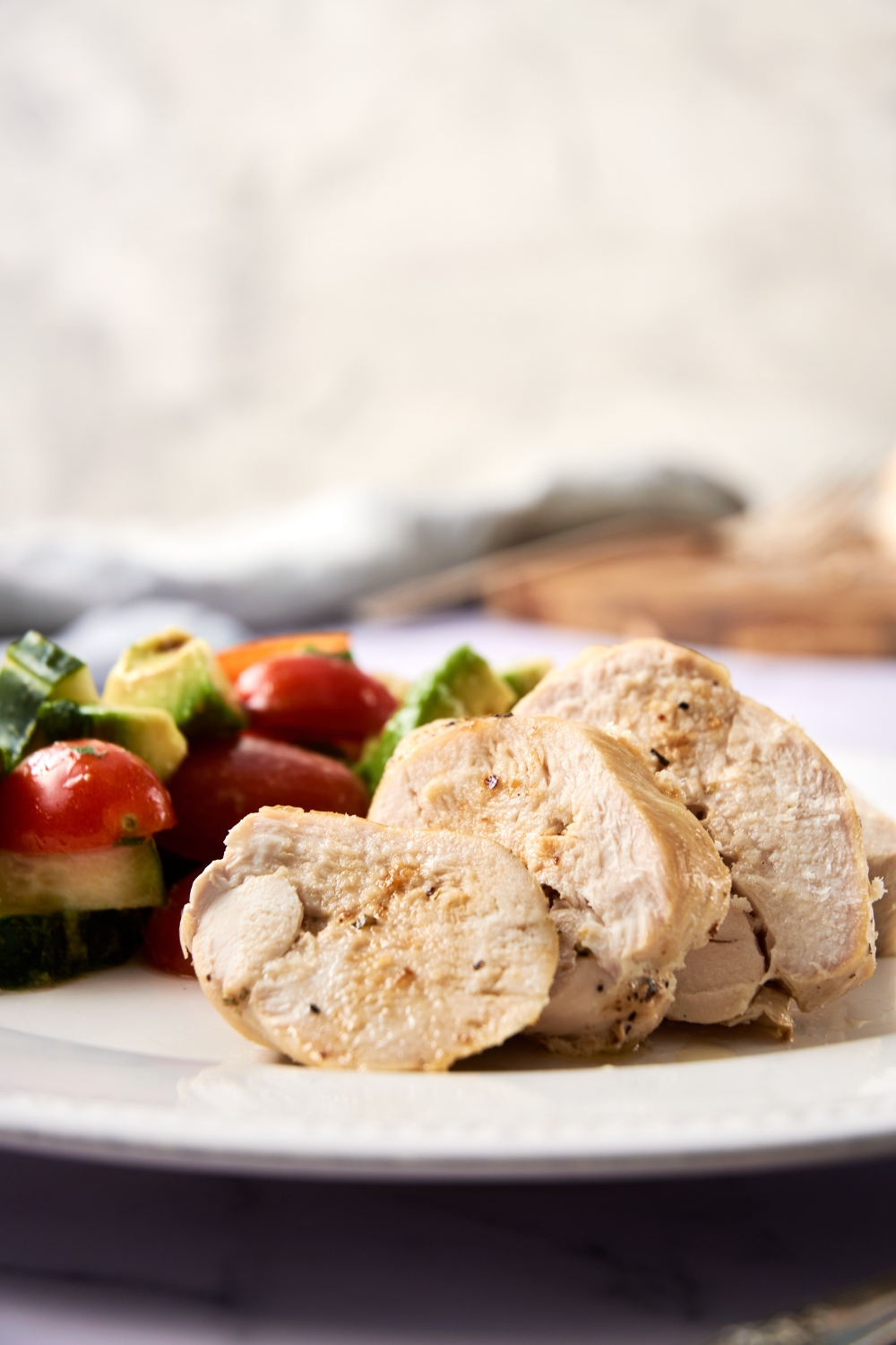 A sliced chicken breast is on a white plate. Vegetables are on the plate as well.